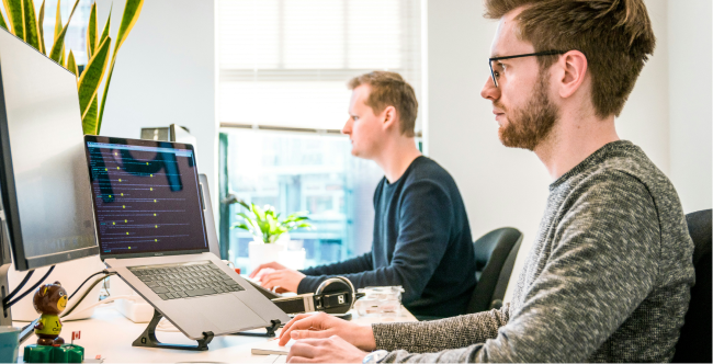 Two persons working in an office in front of computer screens.