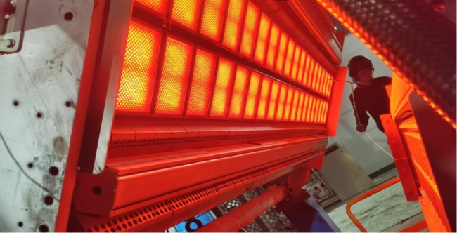 Worker inspecting an active industrial infrared drying system glowing red.